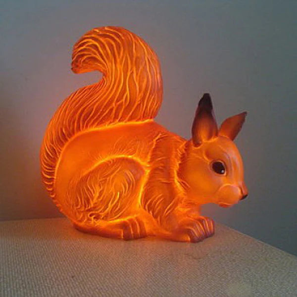 A squirrel shamped lamp. The lamp is on and gives off a soft warm yellow glow.