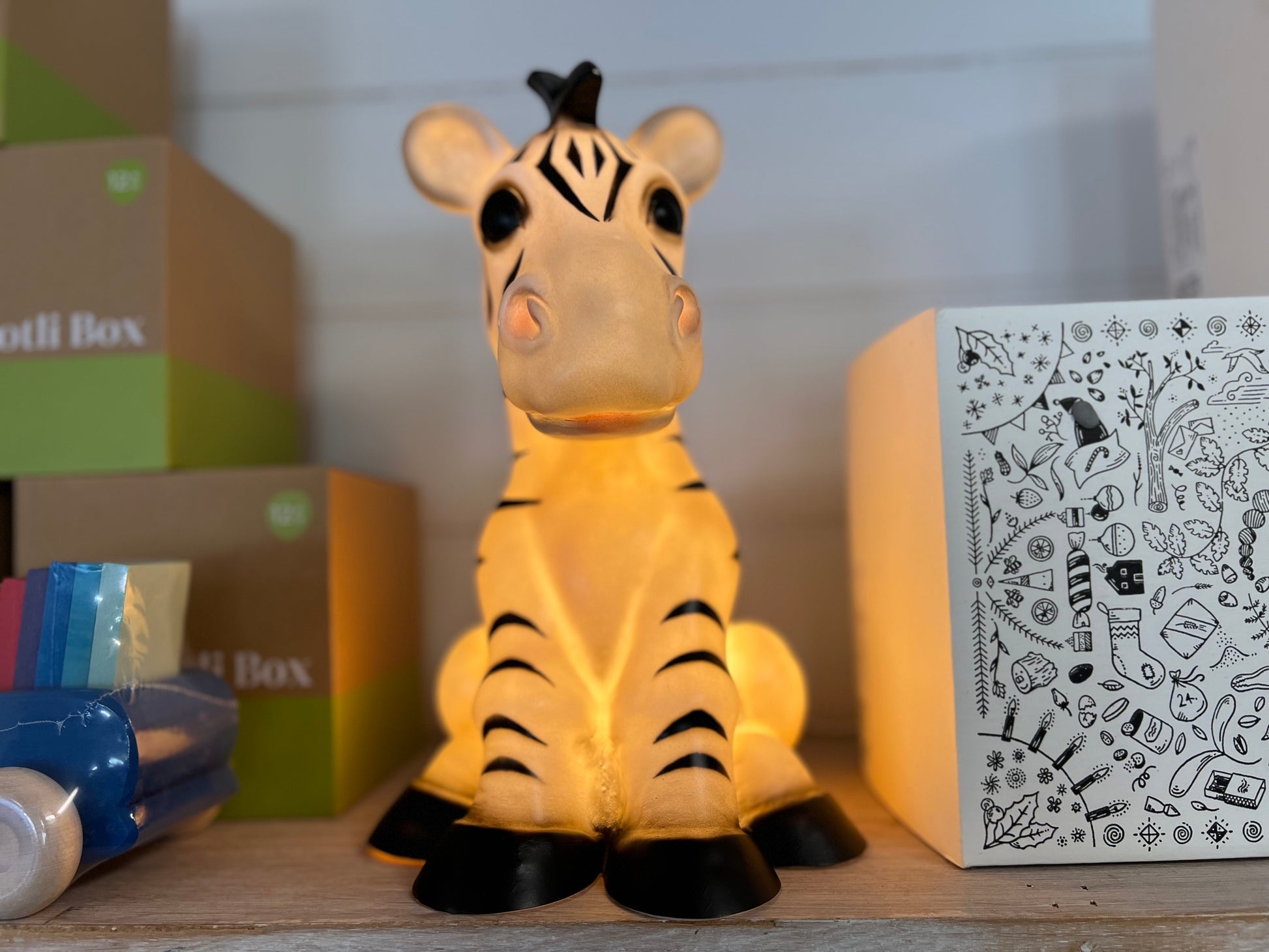 Zebra shaped nightlight facing the camera front on.  The light is on and shows a warm yellow glow.  The Zebra is in a sitting position.