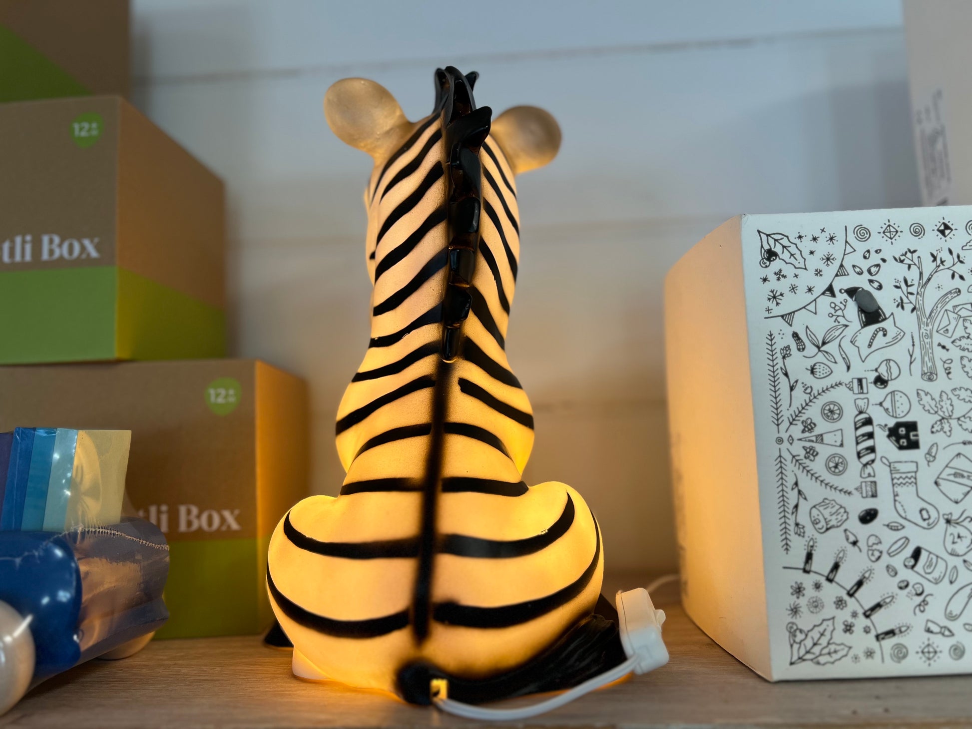 Zebra shaped nightlight facing to the rear.  The light is on and shows a warm yellow glow.  The Zebra is in a sitting position.
